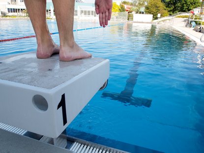 Person steht auf Einser-Startblock in Position, um ins Schwimmbecken im Freibad zu springen.